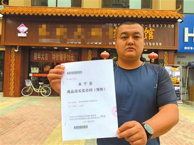 馬先生在自己的營(yíng)業(yè)房前向記者出示他的購(gòu)房合同。